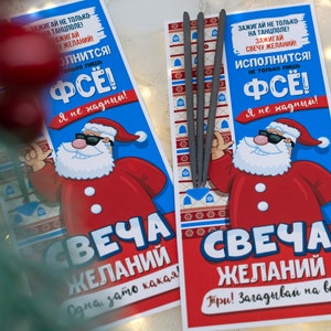 Puede incluir: Dos tarjetas rojas y azules con un Pap&aacute; Noel de dibujos animados que lleva gafas de sol. Las tarjetas tienen el texto "SVECHA ZHELANIY" y "Зажигай не только на танцполе! Зажигай свечу желаний! Исполнится! Не только лишь ФСЁ! Я не хадный!"  Las tarjetas est&aacute;n al lado de un paquete de bengalas plateadas.
