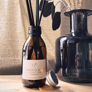 May include: A brown glass reed diffuser bottle with black reeds, a silver cap, and a label that reads "Tobacco & Oak". A dark glass vase is next to the diffuser. The diffuser contains 125ml of liquid.