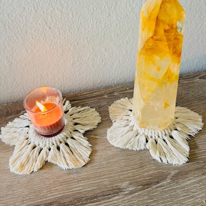 May include: Two white crocheted coasters with fringe, one with a lit orange candle and the other with a large clear crystal with yellow and orange hues.