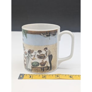 May include: White ceramic mug featuring a picnic scene with a lake, geese, and people. The illustration includes a table with food and a man and woman. The mug has a curved handle and is approximately 4 inches tall.