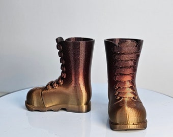 Könnte beinhalten: Ein Paar braune und goldene Stiefel mit Schnürsenkeln. Die Stiefel sind aus einem strukturierten Material gefertigt und haben eine abgerundete Spitze.
