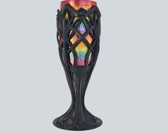May include: A tall, dark vase with an intricate, openwork design. The vase has a flared base and a slender, elongated body. The interior of the vase displays a vibrant, iridescent rainbow of colors, with a red-orange rim.