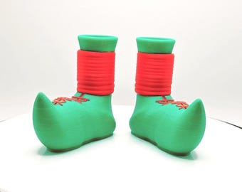 Könnte beinhalten: Ein Paar grüne Elfen-Schuhe mit rotem Besatz. Die Schuhe haben eine spitze Zehenpartie und einen kleinen Absatz.