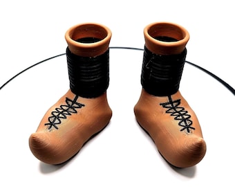 Könnte beinhalten: Ein Paar Terrakotta-Keramikstiefel mit schwarzen Schnürsenkeln und einem schwarzen Band um den oberen Teil jedes Stiefels.