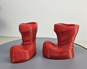 Könnte beinhalten: Zwei rote, 3D-gedruckte, weihnachtliche Stiefel-Blumentopf-Dekorationen. Die Töpfe sind aus glattem, strukturiertem Kunststoff.