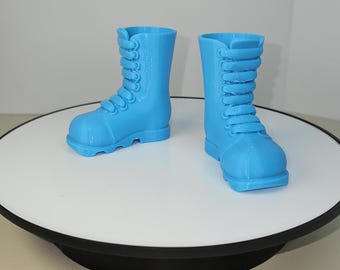 Könnte beinhalten: Ein Paar blaue Plastik-Stiefel mit Schnürsenkeln. Die Stiefel stehen auf einer weißen Oberfläche.