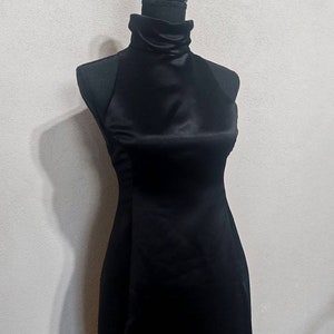 Puede incluir: Un vestido negro de sat&eacute;n con cuello alto y silueta ajustada.