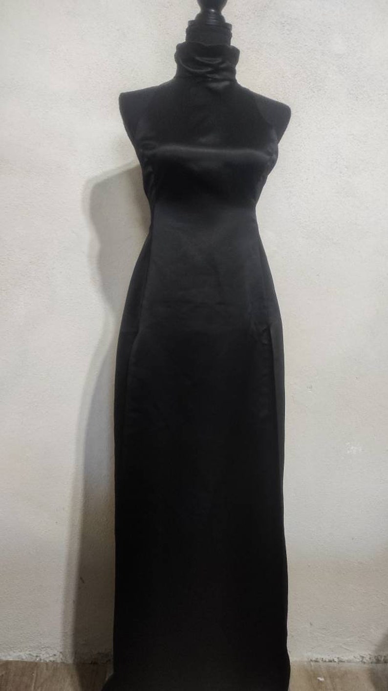 Puede incluir: Un vestido negro de sat&eacute;n con cuello alto y una falda larga y fluida.