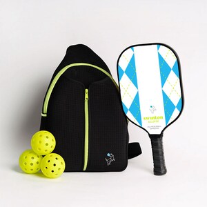 May include: A black pickleball backpack with a neon green zipper and a small dog logo. The backpack is next to three yellow pickleballs and a white and blue pickleball paddle with the text "swinton eclipse USA pickleball approved".