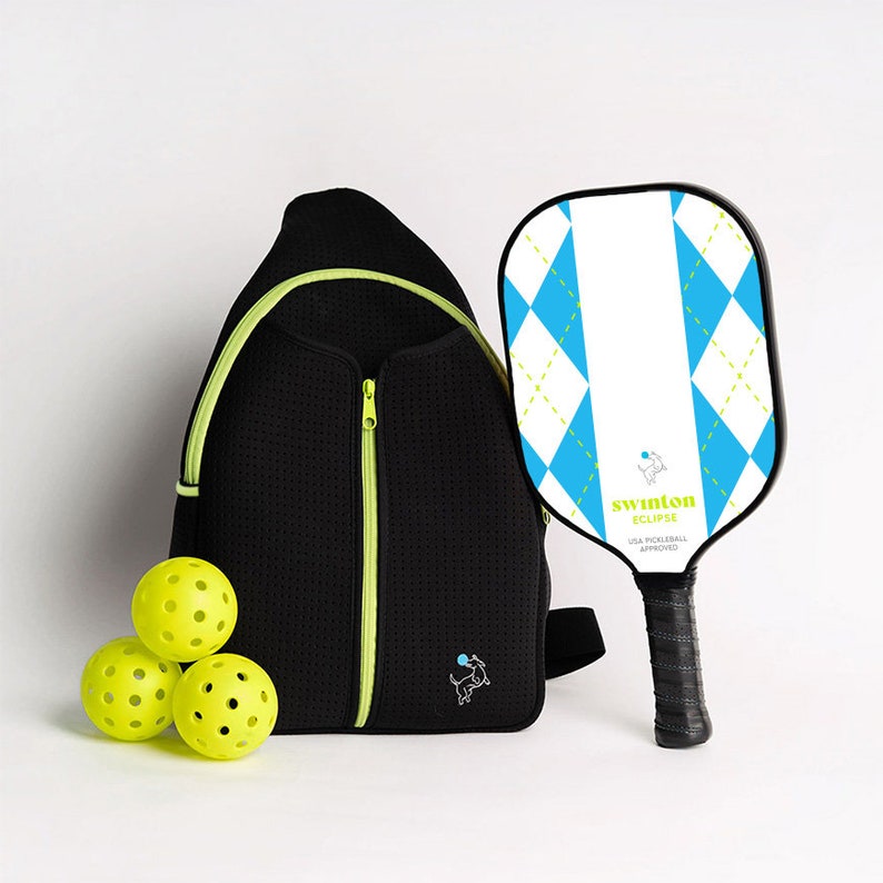 May include: A black pickleball backpack with a neon green zipper and a small dog logo. The backpack is next to three yellow pickleballs and a white and blue pickleball paddle with the text "swinton eclipse USA pickleball approved".