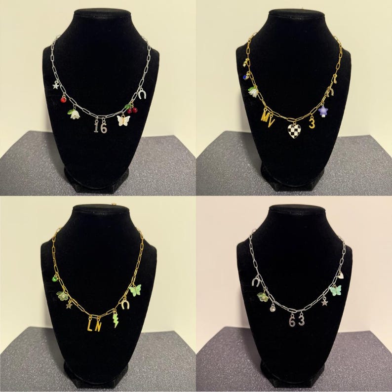 May include: Four silver and gold-toned chain necklaces featuring various charms including butterflies, horseshoes, stars, cherries, flowers, lightning bolts, hearts, and numbers 16, 63, and letters MV and LN, displayed on black jewelry busts.
