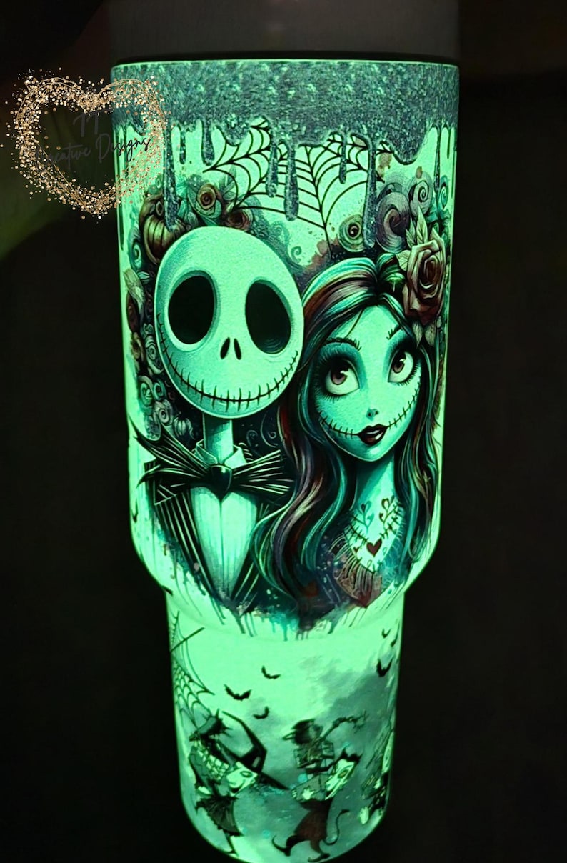 May include: Glow-in-the-dark tumbler featuring Jack Skellington and Sally from The Nightmare Before Christmas. The design includes cobwebs, bats, and a heart tattoo. The tumbler has a teal and black color scheme.