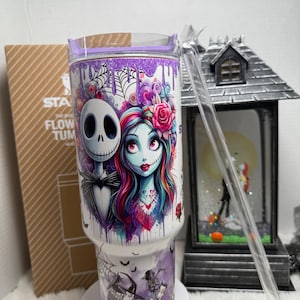 May include: A white tumbler with a purple lid and straw features Jack Skellington and Sally from The Nightmare Before Christmas. The design includes a watercolor style image of the characters, spiderwebs, and bats. The tumbler has the text "STA FLOW TUM".