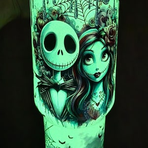 May include: A glowing green tumbler featuring Jack Skellington and Sally from The Nightmare Before Christmas. The design includes cobwebs, bats, and other spooky elements. The tumbler is a vibrant, eye-catching accessory.