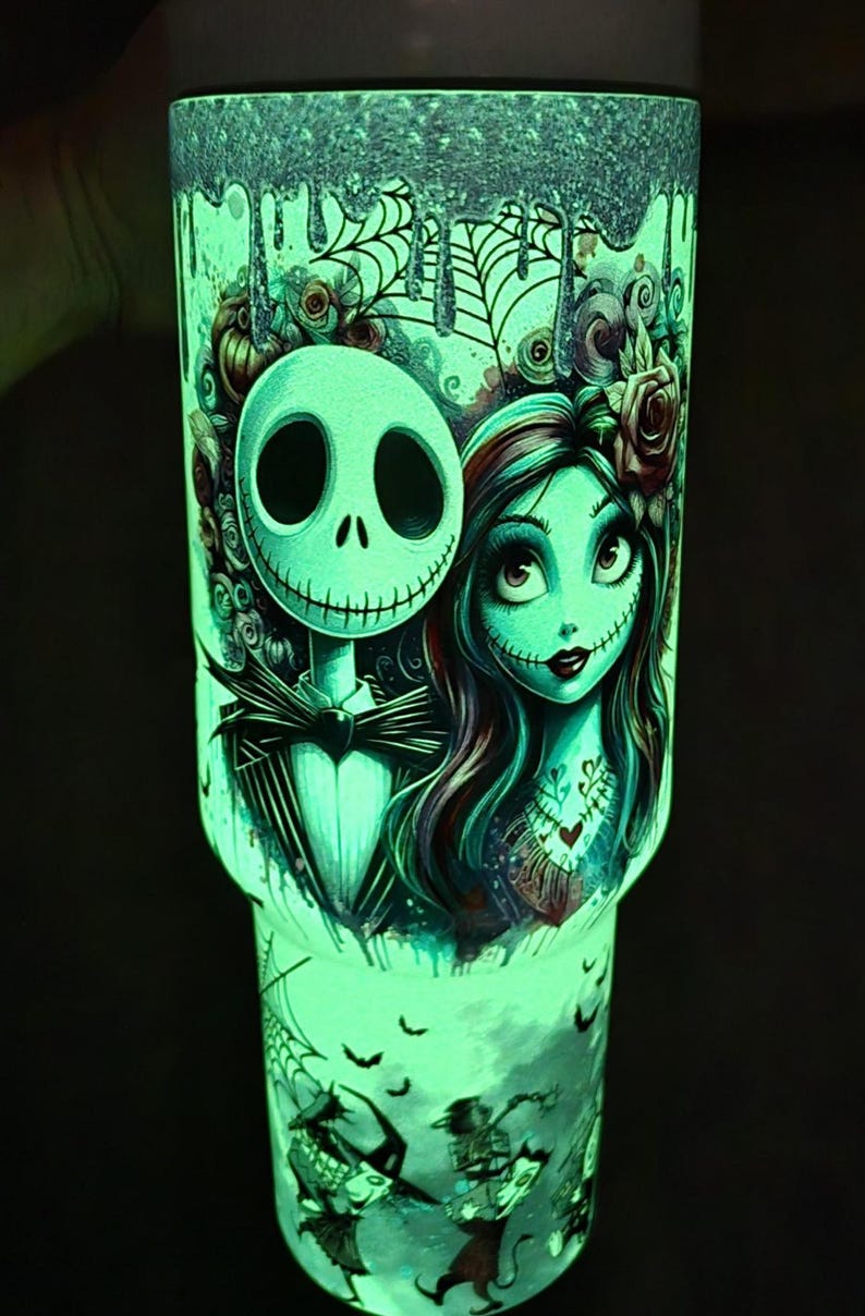 May include: A glowing green tumbler featuring Jack Skellington and Sally from The Nightmare Before Christmas. The design includes cobwebs, bats, and other spooky elements. The tumbler is a vibrant, eye-catching accessory.
