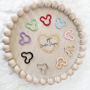 May include: A collection of ten Mickey-shaped spring gate rings in various colors including red, light blue, light green, purple, black, silver, gold, pink, and peach, arranged in a circle around the text TT Creative Designs.