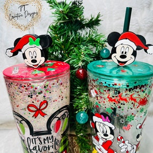 May include: Two clear plastic tumblers with glitter and Christmas-themed designs. One tumbler features Mickey Mouse and Minnie Mouse in Santa hats, with the text "It's my favorite time of the year". The other tumbler features Mickey Mouse and Minnie Mouse in Santa hats, with a red and green candy cane design.