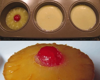 May include: A close-up of a baked pineapple upside-down cake with a red maraschino cherry on top. The cake is in a baking pan with other cakes in the background.