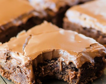 Pode incluir: Um close-up de um brownie de chocolate com uma mordida tirada. O brownie é coberto com uma camada de cobertura de chocolate.