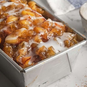 May include: A loaf of apple cinnamon bread topped with a white glaze in a silver loaf pan.