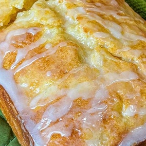 Op de afbeelding: Een citroenbrood met een witte glazuur eroverheen gedruppeld. Het brood ligt op een groene theedoek.