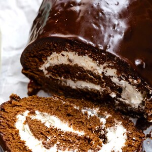 May include: A chocolate cake roll with a chocolate glaze and white frosting filling. The cake roll is sliced and the inside is visible.
