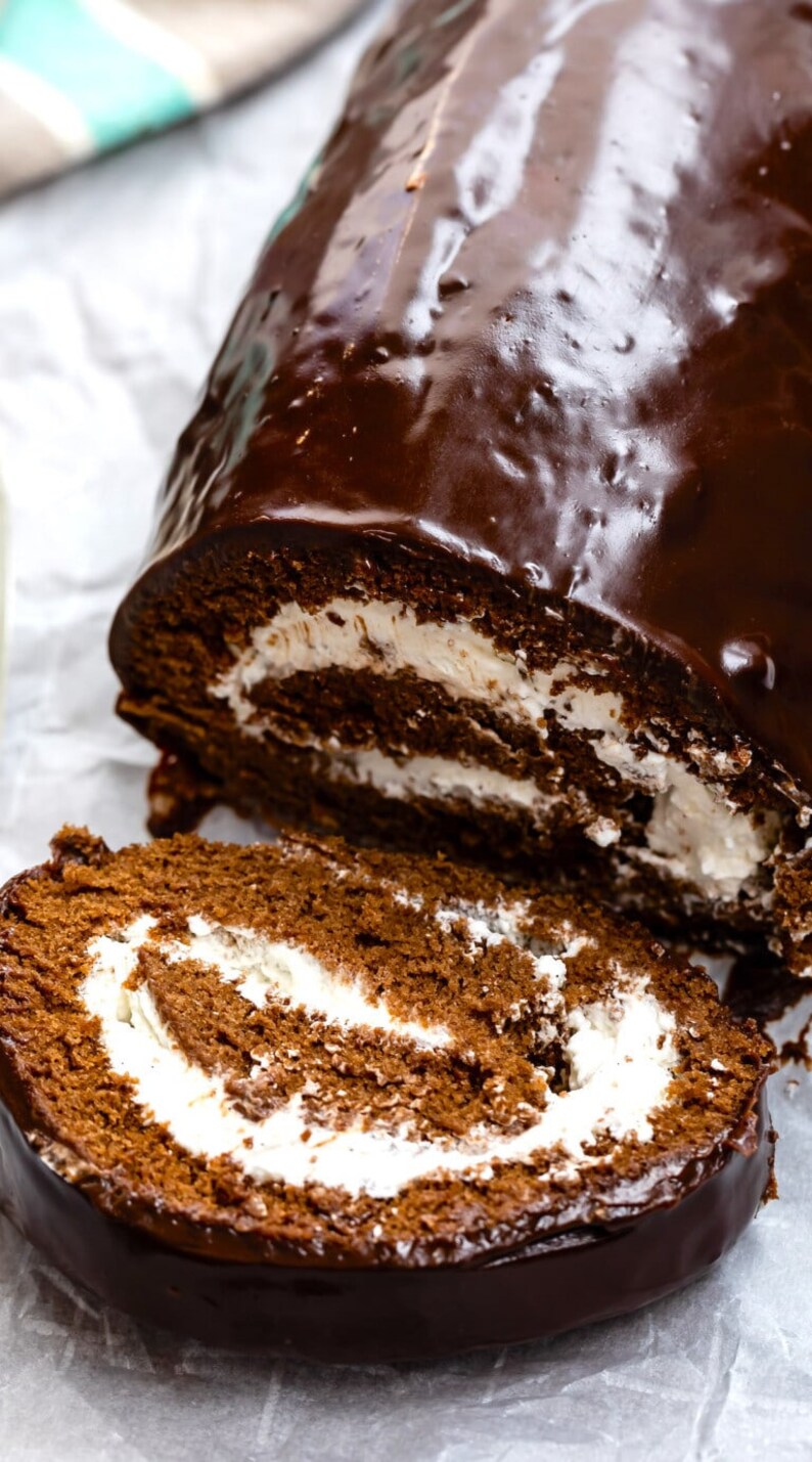 May include: A chocolate cake roll with a chocolate glaze and white frosting filling. The cake roll is sliced and the inside is visible.