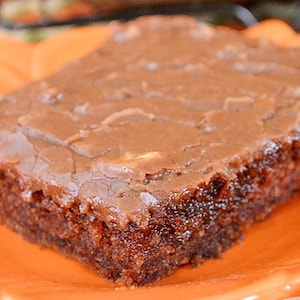 以下が含まれることがあります： チョコレートの厚い層で覆われたチョコレートケーキのクローズアップ。ケーキは茶色とオレンジの皿の上にある。