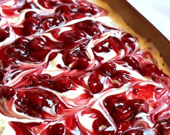 May include: A white and red dessert with a swirl pattern. The dessert is in a brown baking dish. The dessert is topped with red cherry pie filling.