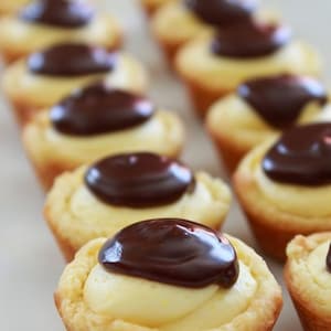 Könnte beinhalten: Nahaufnahme einer Reihe von Mini-Desserts mit einer gelben Puddingfüllung, die mit einer dunklen Schokoladen-Ganache überzogen ist.