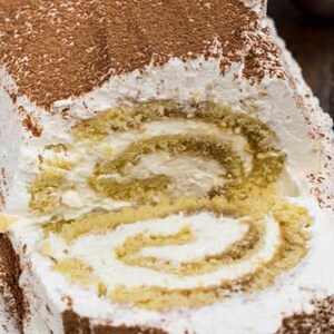 May include: A close-up of a chocolate-covered yule log cake with a white whipped cream frosting and a slice cut out to reveal the layers of cake and filling.