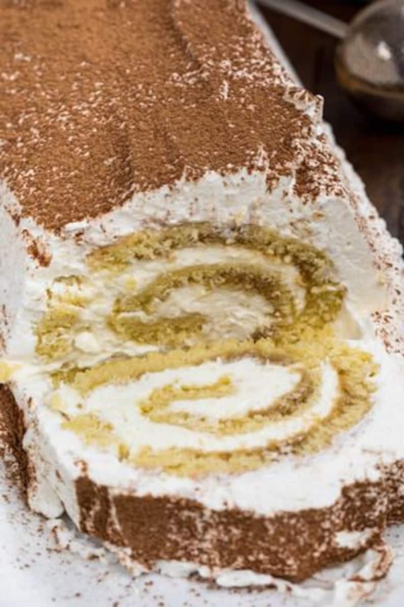 May include: A close-up of a chocolate-covered yule log cake with a white whipped cream frosting and a slice cut out to reveal the layers of cake and filling.