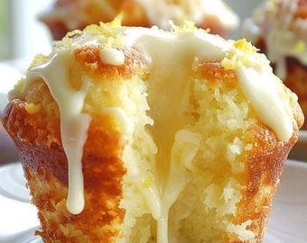 May include: Close-up of a lemon cupcake with a white frosting and a lemon glaze. The cupcake is split in half, revealing the moist yellow cake inside.