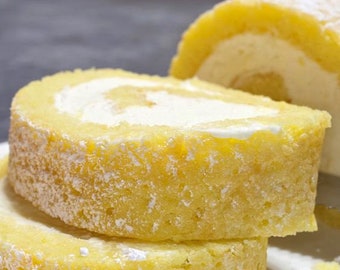以下が含まれることがあります： 粉砂糖をまぶした黄色いロールケーキのクローズアップ。ロールケーキはスライスされ、白い皿に重ねられています。手前に粉砂糖を入れた小さな銀製のふるいがあります。
