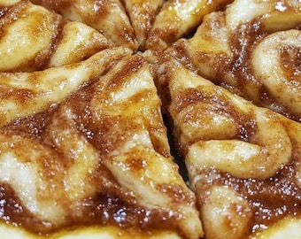 Peut inclure: Une pizza au pain d'épices coupée en tranches. La pizza est garnie d'un tourbillon de cannelle brun et d'un glaçage blanc. La croûte est dorée.