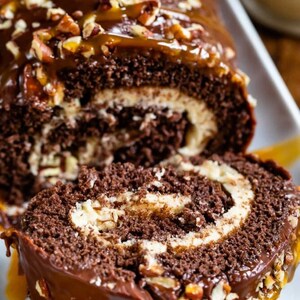 May include: A chocolate cake roll with a white cream filling, topped with chocolate frosting, caramel sauce, and chopped pecans.