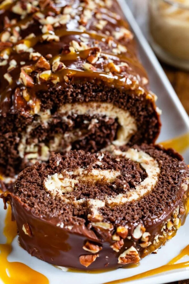 May include: A chocolate cake roll with a white cream filling, topped with chocolate frosting, caramel sauce, and chopped pecans.