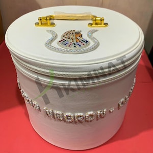 May include: White round storage box with a gold handle and a decorative design of a woman with jewels on the lid. The box has a zipper closure and the words "FORBIDDEN" are spelled out in rhinestones around the bottom.