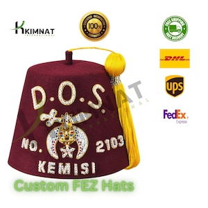 Puede incluir: Un fez granate con ribetes dorados y un borlón amarillo. El sombrero tiene un emblema blanco y dorado con el texto "D.O.S. NO. 2103 KEMISI" en la parte delantera.