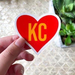 May include: Red heart-shaped sticker with a white outline and the text "KC" in yellow letters.