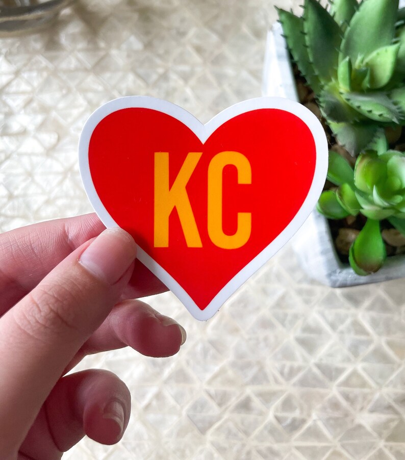 May include: Red heart-shaped sticker with a white outline and the text "KC" in yellow letters.