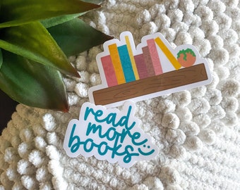 Peut inclure: Un autocollant blanc avec le texte "read more books" en lettres bleu turquoise. L'autocollant est sur une surface blanche et duveteuse. Un deuxième autocollant est visible en arrière-plan, représentant une étagère avec des livres colorés et une petite plante en pot.