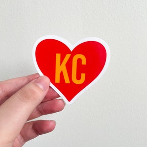 May include: Red heart-shaped sticker with a white outline and the text "KC" in yellow.