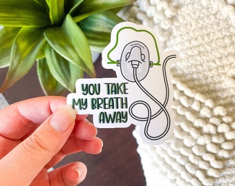 Könnte beinhalten: Ein weißer Aufkleber mit grünem Rand zeigt eine Cartoon-Zeichnung einer Sauerstoffmaske mit dem Text "You take my breath away".
