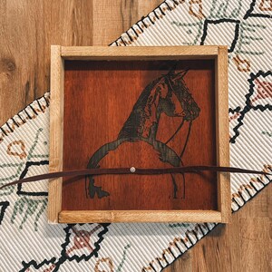 May include: A wooden tray with a dark brown stain features a laser-etched silhouette of a horse's head and neck. The tray has a leather strap across the top.