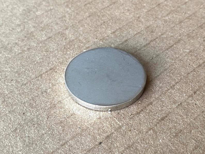 May include: A silver-coloured metal disc with a smooth surface.