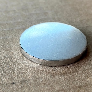 May include: A silver-coloured metal disc with a smooth, slightly textured surface. The disc has a slightly raised edge.