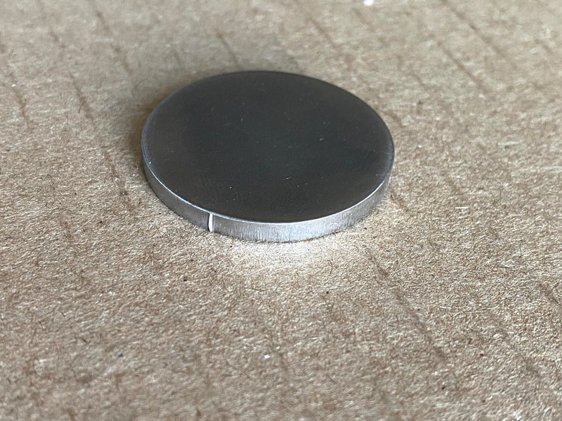 May include: A silver-colored metal disc with a smooth, polished surface.