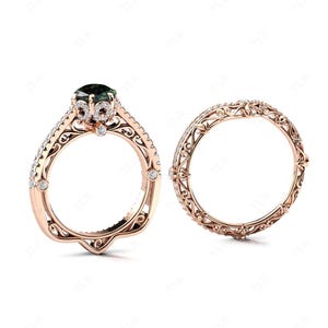 Puede incluir: Un juego de anillo de compromiso y alianza de oro rosa. El anillo de compromiso presenta una piedra preciosa verde oscuro y detalles de filigrana intrincados. La alianza tiene un diseño de filigrana a juego y pequeñas piedras de acento. Ambos anillos están sobre un fondo blanco.
