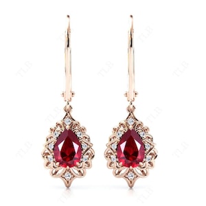 May include: A pair of drop earrings featuring a pear-shaped ruby gemstone surrounded by smaller diamonds in a delicate filigree setting. The earrings are crafted from rose gold.